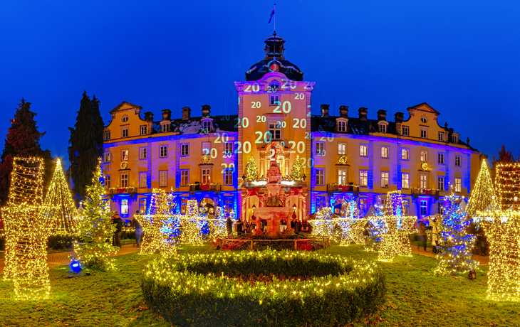 Festlich beleuchtetes Schloss mit Weihnachtsdekoration und blauen Abendhimmel.