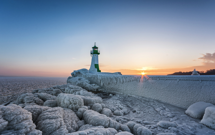 Vereister Leuchtturm bei Sonnenuntergang am Hafen von Sassnitz, Insel Rügen.