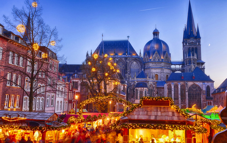 Weihnachtsmarkt mit Dom im Hintergrund bei Abenddämmerung.