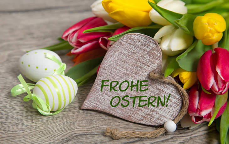 Tulpen und Holzherz mit Frohe Ostern, daneben dekorierte Ostereier.