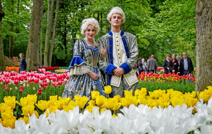 Personen in historischer Kleidung im Keukenhof mit Tulpen im Hintergrund.