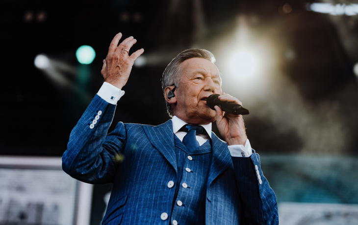 Mann in Anzug singt auf einer beleuchteten Bühne.