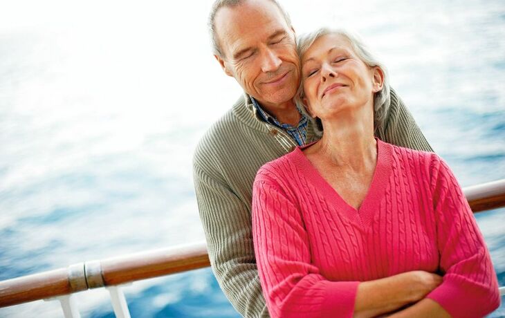 Älteres Paar umarmt sich auf einem Schiff vor blauem Meer.