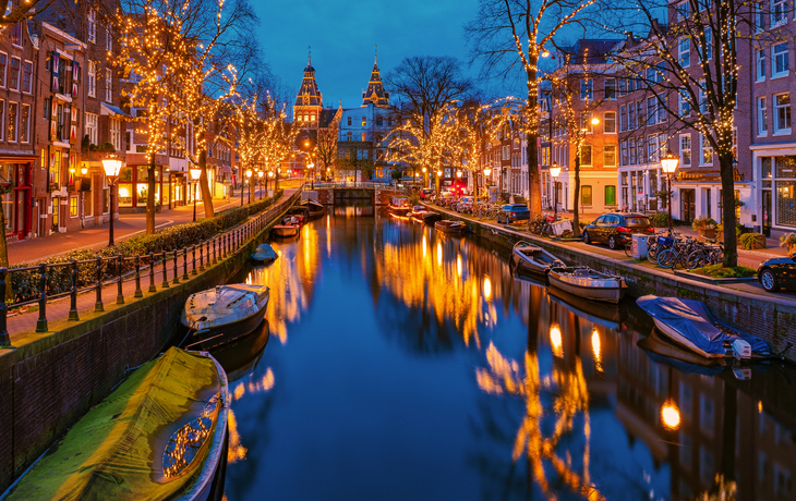 Amsterdamer Kanal im Winter mit festlicher Weihnachtsbeleuchtung und Booten am Ufer.
