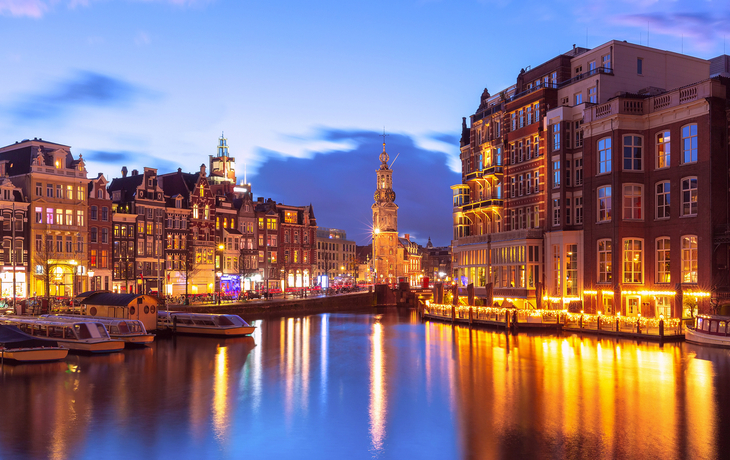 Stimmungsvolle Kanalansicht in Amsterdam bei Abenddämmerung mit beleuchteten Gebäuden.
