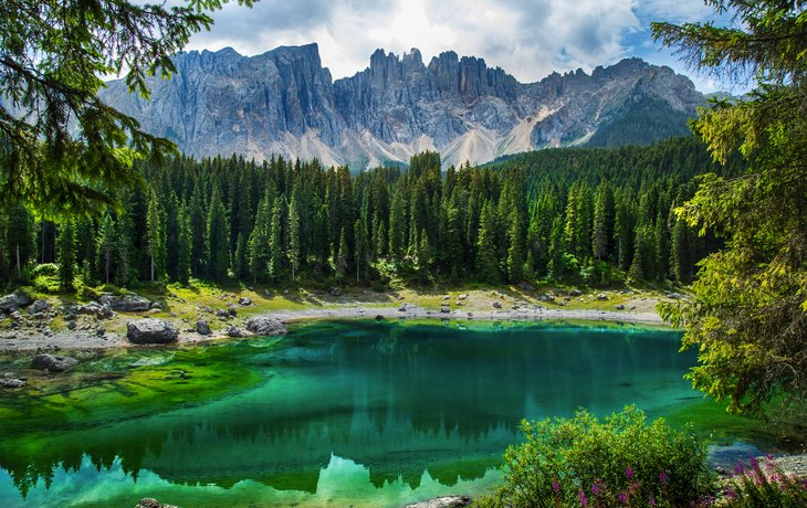 Karersee in den Dolomiten, umgeben von Wald und Bergen, unter blauem Himmel.