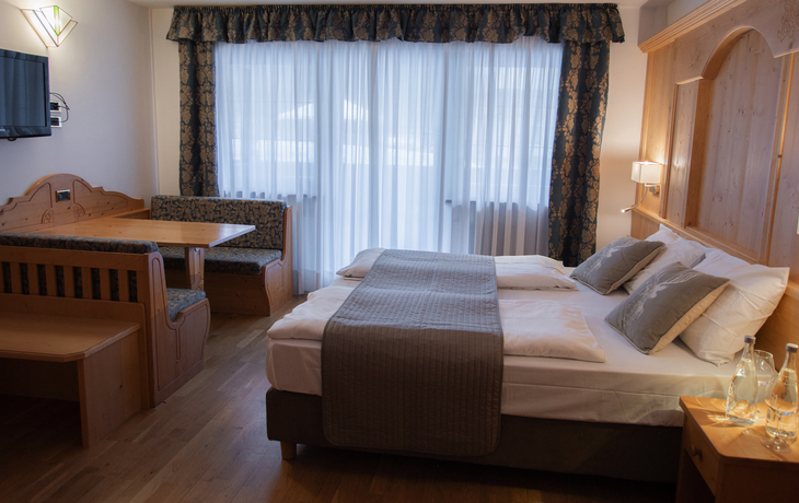 Doppelzimmer mit Doppelbett, Holzmöbeln und Sitzbereich in einem Hotel.