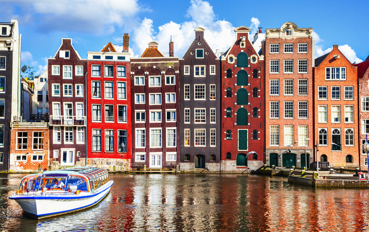 Grachtenhäuser und Ausflugsboot in Amsterdam bei Sonnenschein.