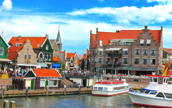 Bunte Holzhäuser und Boote im Hafen von Volendam bei sonnigem Wetter.
