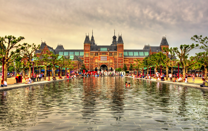Blick auf das Rijksmuseum in Amsterdam mit Wasserkanal im Vordergrund.