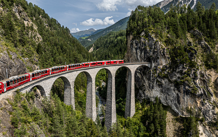 Roter Zug auf dem Landwasserviadukt in einer bewaldeten Berglandschaft.
