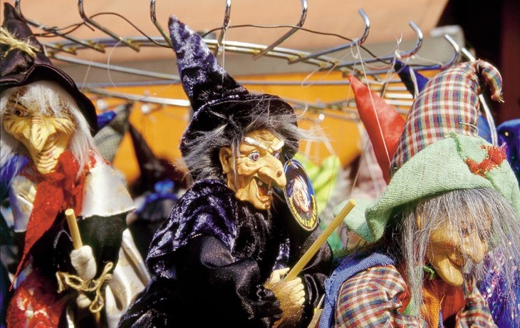 Hexenpuppen in bunter Kleidung mit Hüten auf einem Marktständer.