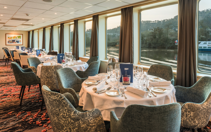 Elegantes Restaurant mit gedeckten Tischen und großen Fenstern mit Seeblick.