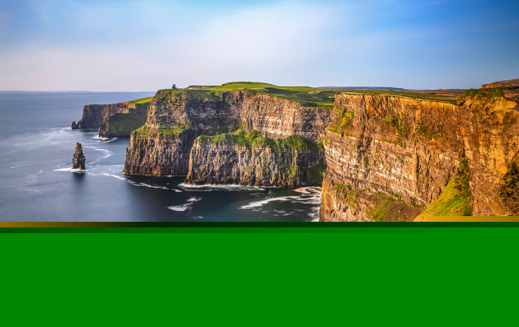 Klippenlandschaft am Meer mit grüner Grasfläche und klarem Himmel.