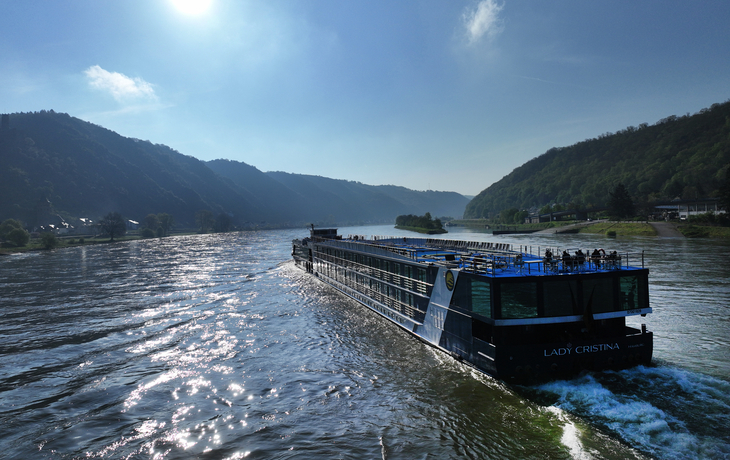 Kreuzfahrtschiff MS Lady Cristina auf einem Fluss zwischen bewaldeten Hügeln.