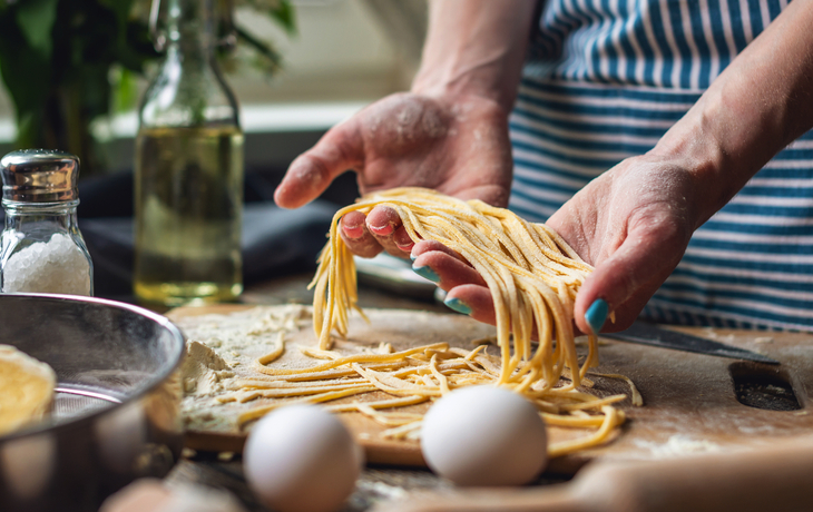 Person macht frische Pasta auf einem Holzbrett in der Küche