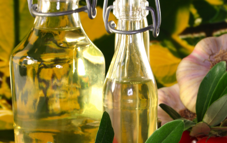 Flaschen mit Olivenöl, frische Oliven, Tomaten und Knoblauch auf einem Tisch.