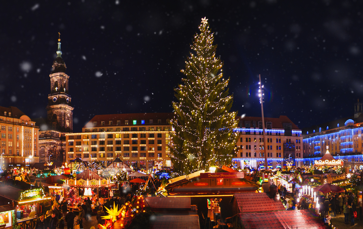 Weihnachtsmarkt in Dresden mit Lichtern und Weihnachtsbaum nachts unter Schneefall