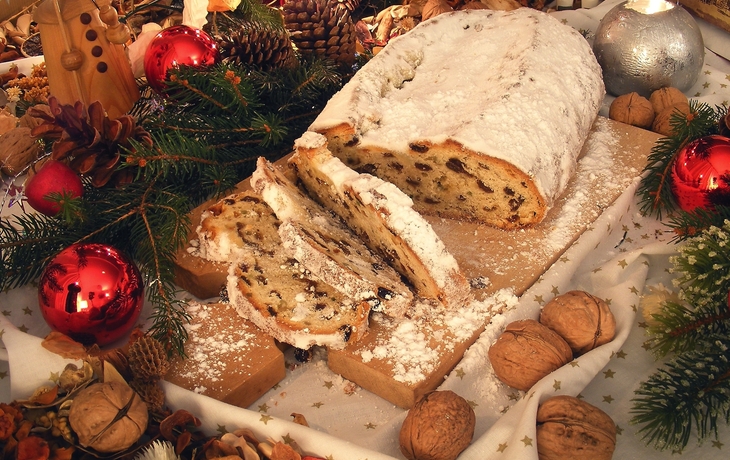 Christstollen mit Puderzucker auf Holzbrett, umgeben von weihnachtlicher Dekoration.