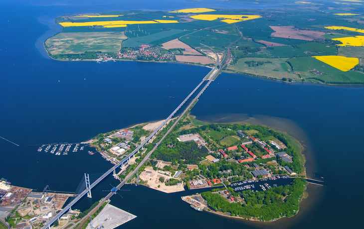 Luftaufnahme einer Brücke über ein Gewässer mit umliegenden Feldern und Häusern.