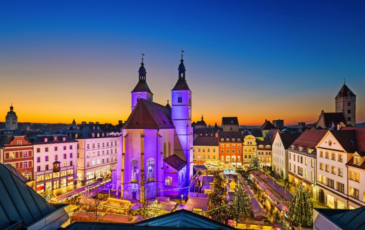 Weihnachtsmarkt bei Abenddämmerung in historischer Altstadt mit beleuchteter Kirche.