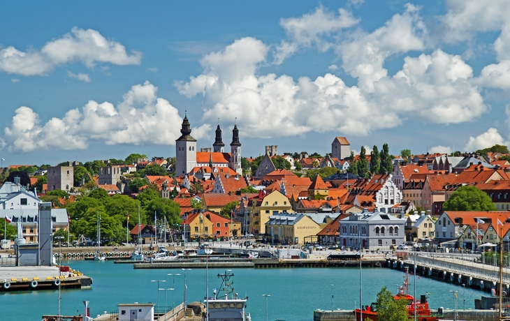 Hafenstadt mit farbenfrohen Gebäuden und Kirchtürmen im Hintergrund, unter blauem Himmel.