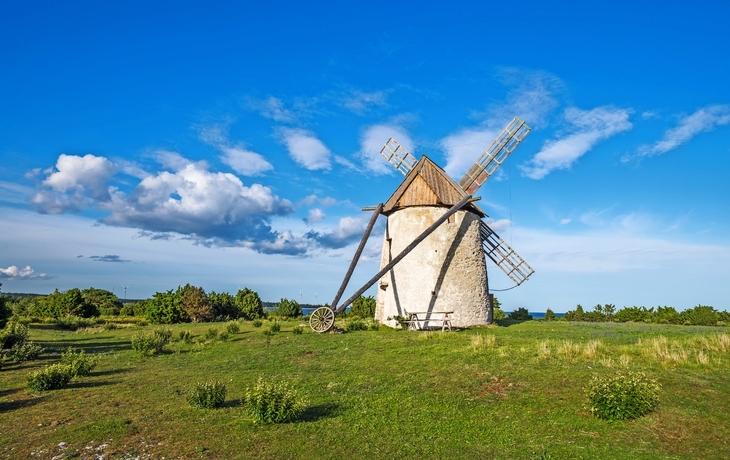 Eine alte Windmühle steht auf einem grünen Feld unter einem blauen Himmel mit weißen Wolken.
