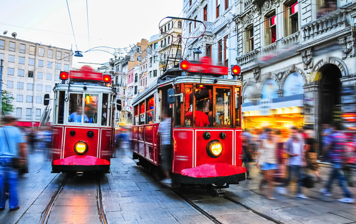 Zwei rote Straßenbahnen fahren durch eine belebte städtische Straße.
