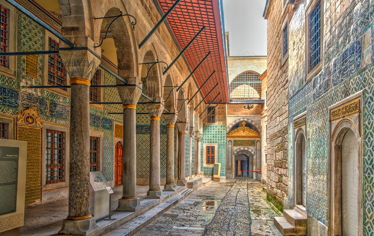 Historischer Innenhof mit verzierten Säulen und bunter Fliesenwand.