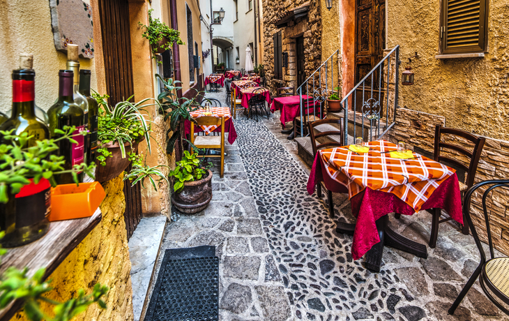 Enge Gasse mit Tischen und Stühlen vor einem Restaurant.