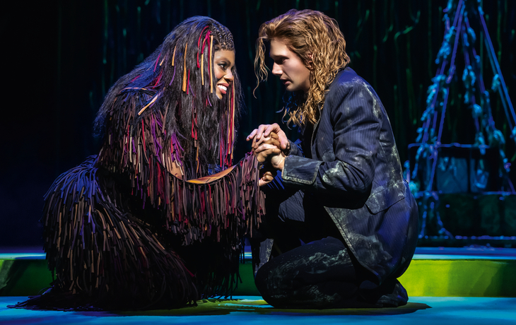 Zwei Personen knien sich gegenüber auf der Bühne und halten einander die Hände.