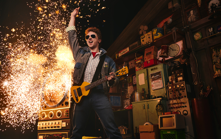 Person in einem Labor mit Gitarre, umgeben von Funken.