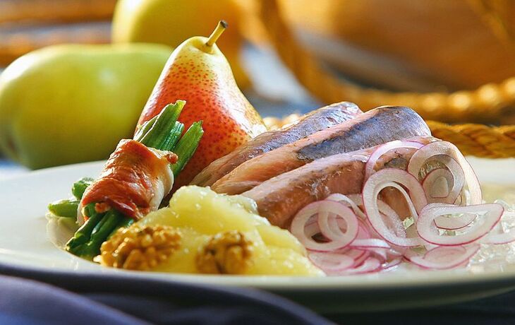 Ein Teller mit Fleisch, grünen Bohnen im Speckmantel, Zwiebeln, Birne und Walnusspüree.