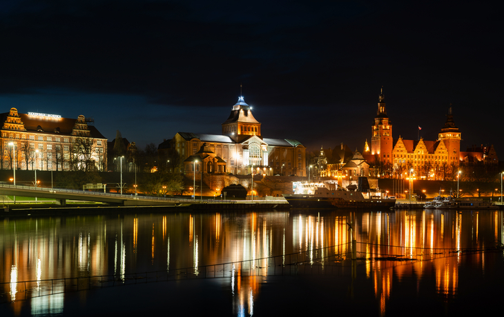 Abendpanorama von Szczecin in Polen© Mike Mareen - stock.adobe.com Nachtsicht auf beleuchtete Gebäude und deren Spiegelung in einem Fluss.