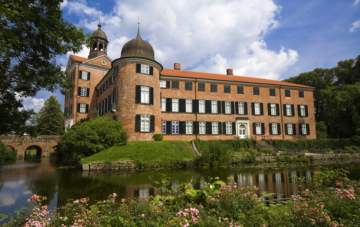 Historisches Schloss aus Backstein mit Turm und Wassergraben an einem sonnigen Tag.