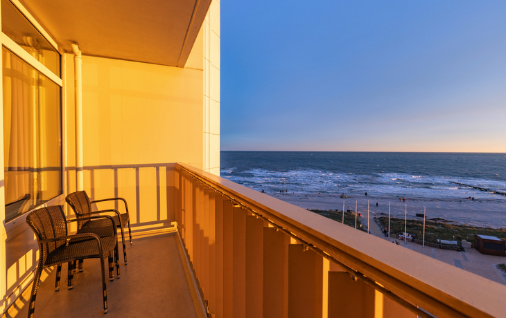 Blick von einem Balkon auf den Strand und das Meer bei Sonnenuntergang.
