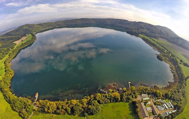 Luftaufnahme eines großen, kreisförmigen Sees, umgeben von Wäldern und Feldern.