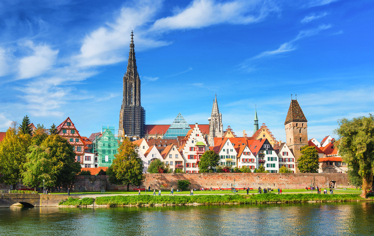 Stadtansicht am Fluss mit historischer Architektur und Kirchturm unter blauem Himmel