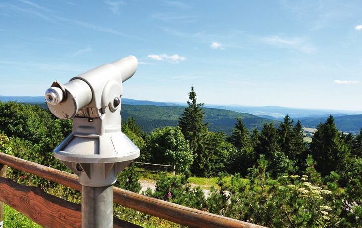 Aussichtsfernrohr mit Blick auf bewaldete Hügel und blauen Himmel.