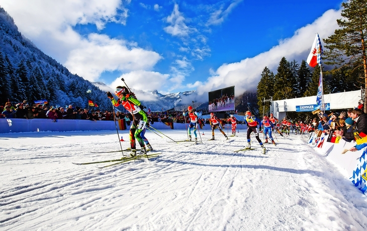 Damen-Biathlon-Starterfeld auf schneebedeckter Strecke mit Zuschauern.
