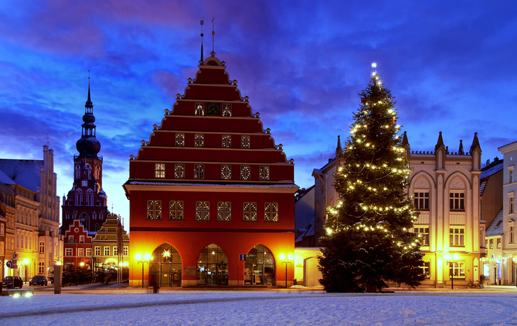 Verschneiter Marktplatz in Greifswald mit Weihnachtsbeleuchtung und historischem Gebäude.