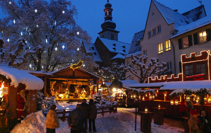 Weihnachtsmarkt mit geschmückten Ständen und schneebedeckten Häusern in der Abenddämmerung.