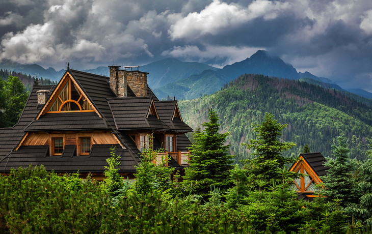 Haus in Berglandschaft mit bewölktem Himmel und grünen Bäumen.