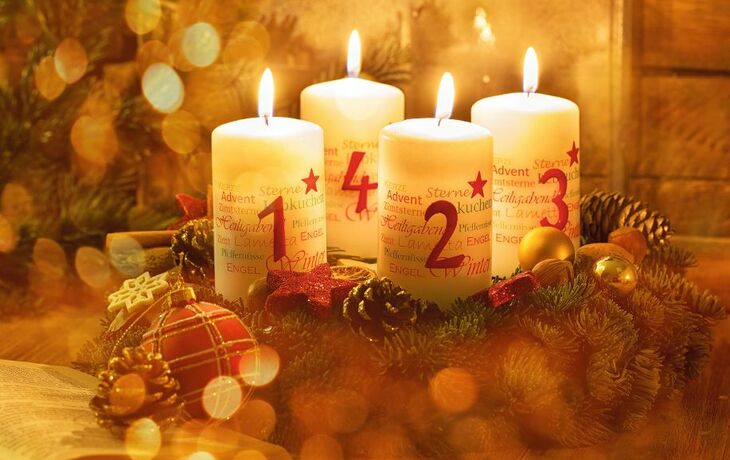 Adventskranz mit vier brennenden Kerzen und weihnachtlicher Dekoration.