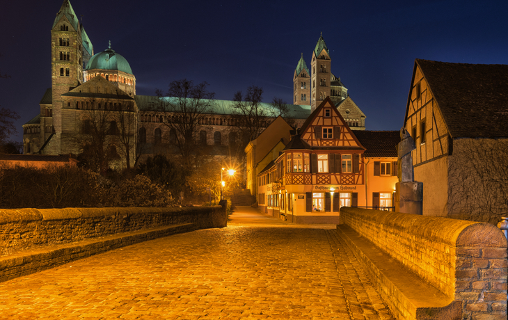 Pflasterstraße in der Nacht vor einer beleuchteten Kathedrale und Fachwerkhäusern.