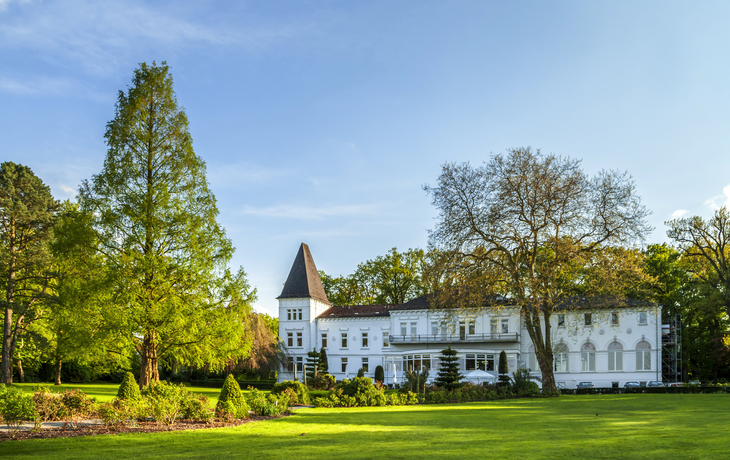 Altes Kurhaus Bad Zwischenahn im Grünen mit Bäumen und klarer Himmel.