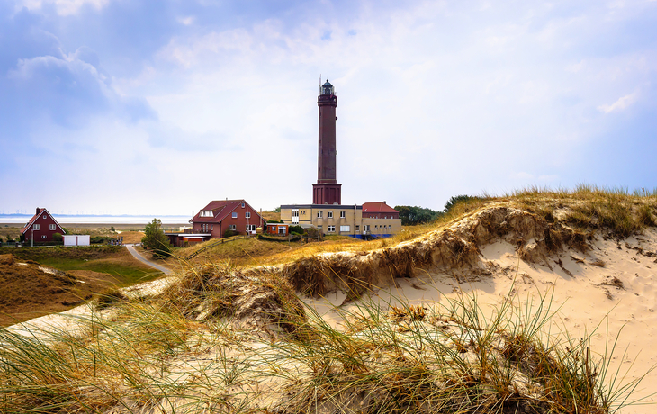 Leuchtturm auf der Insel Norderney mit Sanddünen im Vordergrund und Meer im Hintergrund.