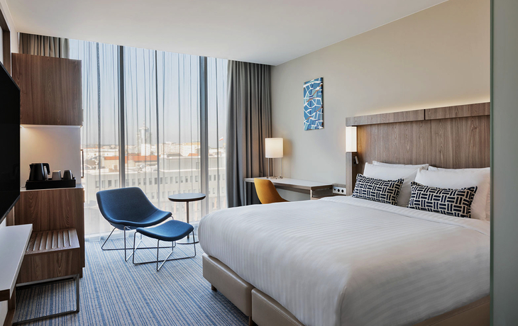 Modernes Hotelzimmer mit Kingsize-Bett, Schreibtisch und Stadtblick.