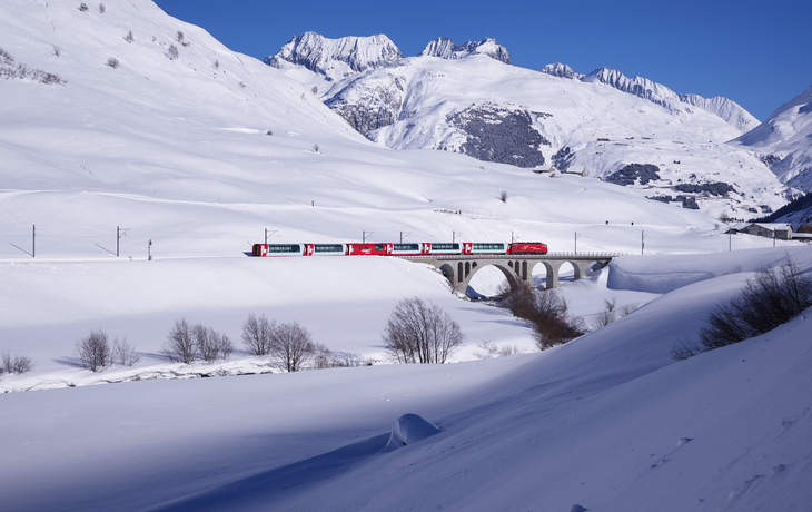 Glacier Express fährt im Winter durch die verschneiten Alpen nach Andermatt.