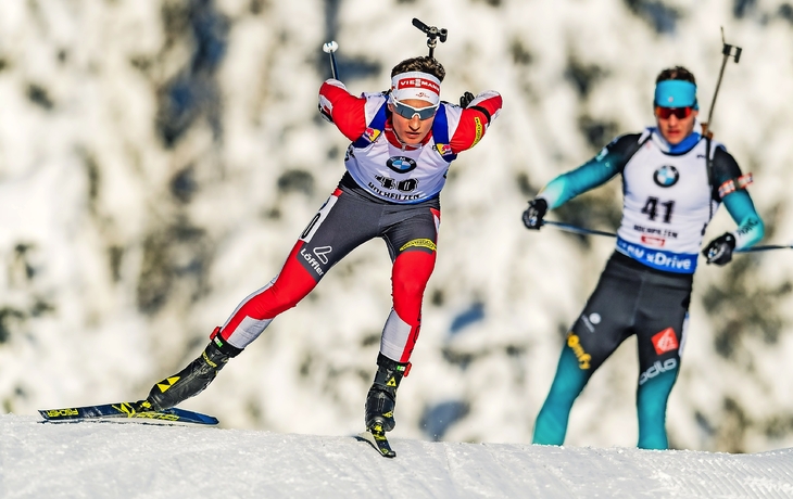 Biathleten im Rennen bei sonnigem Wetter auf schneebedeckter Strecke.